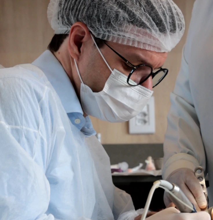 Cirurgião-dentista paramentado com touca, máscara e avental durante atendimento clínico